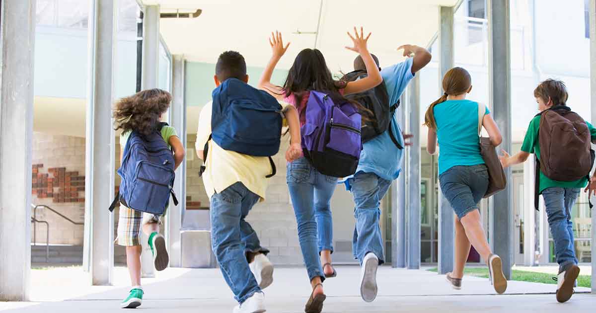 Una fila de niños con mochilas corriendo emocionados hacia su escuela.