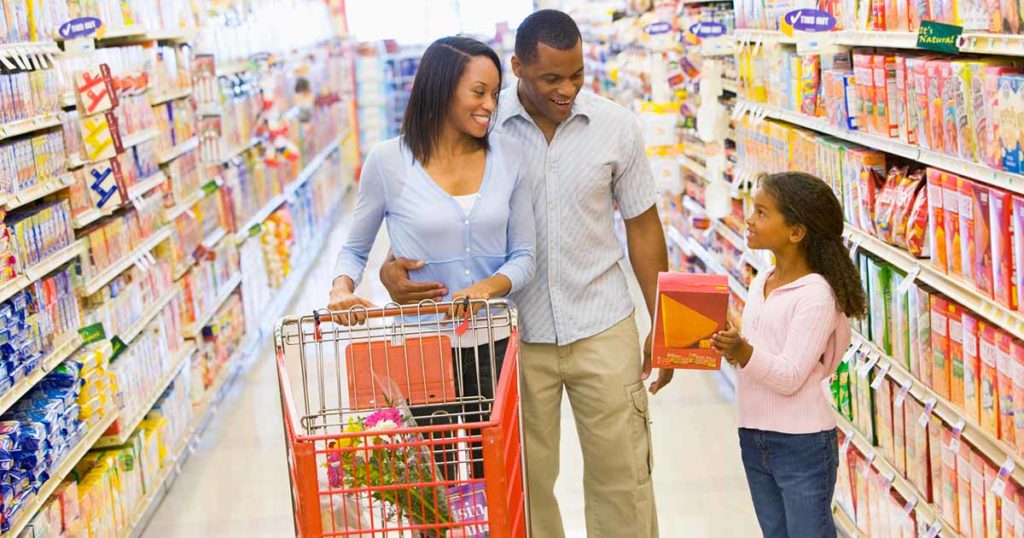 Familia comprando en el pasillo del supermercado en busca de alimentos asequibles y libres de alérgenos.