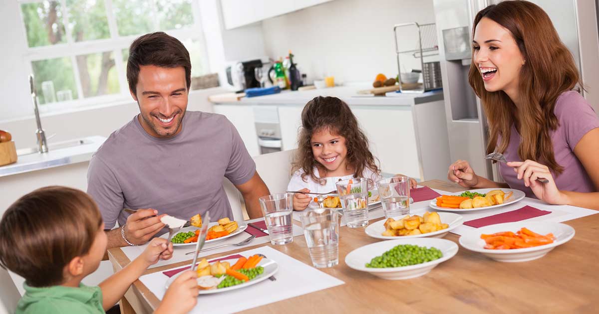 Familia sentada en la mesa de su cocina disfrutando de una cena amigable con los alérgenos.