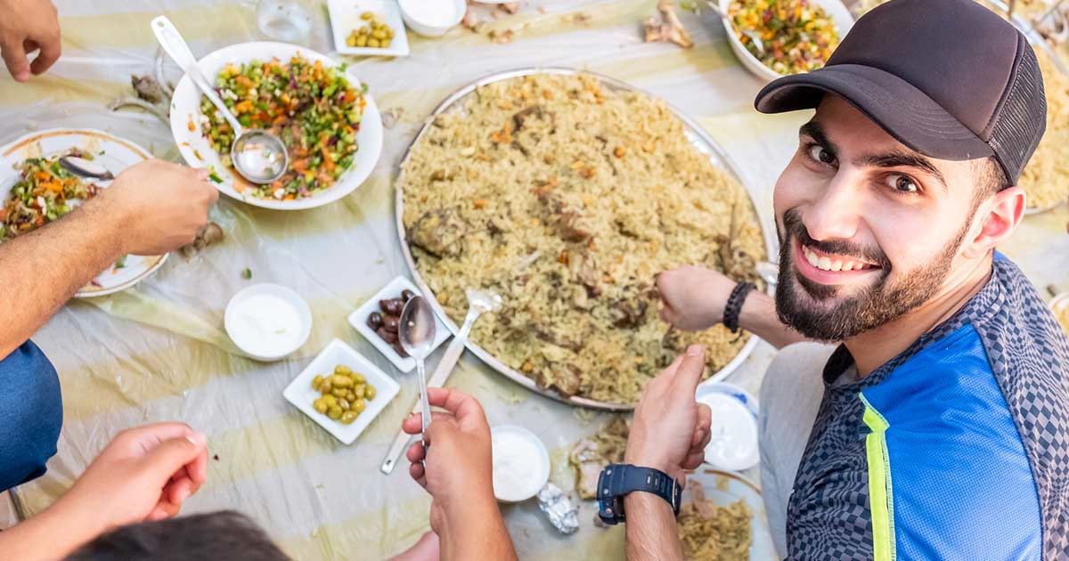 Musulmán feliz en la mesa con su familia disfrutando de una comida étnica cocinada sin alérgenos alimentarios.